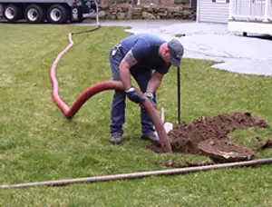 Septic pumping technician servicing a residential septic tank with a vacuum hose in Durham, NC