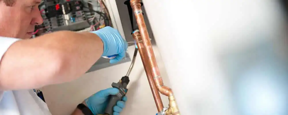 Water heater repair technician testing copper pipe connections and controls in Durham, NC